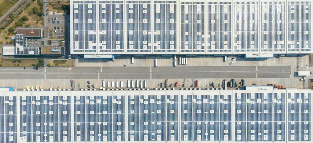 An aerial view of large warehouse roofs covered in solar panels with loading docks