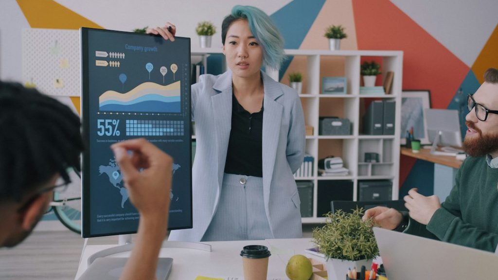 A woman with blue hair presenting a growth chart to colleagues in an office
