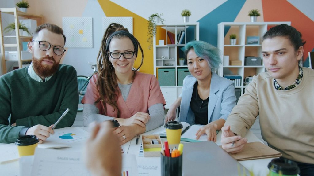 Four people sitting at a desk in a colorful office during a meeting