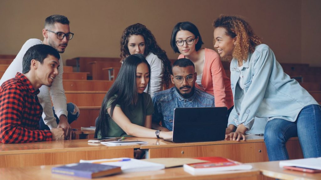 Diverse group of students gathered around a laptop